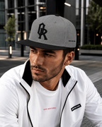 A man wearing a grey and black Off-Record snapback cap and a white zip-up jacket with black trim in an outdoor urban setting.