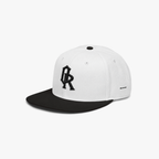 White and black snapback cap with a black embroidered 'OR' logo on the front, set against a plain light gray background.
