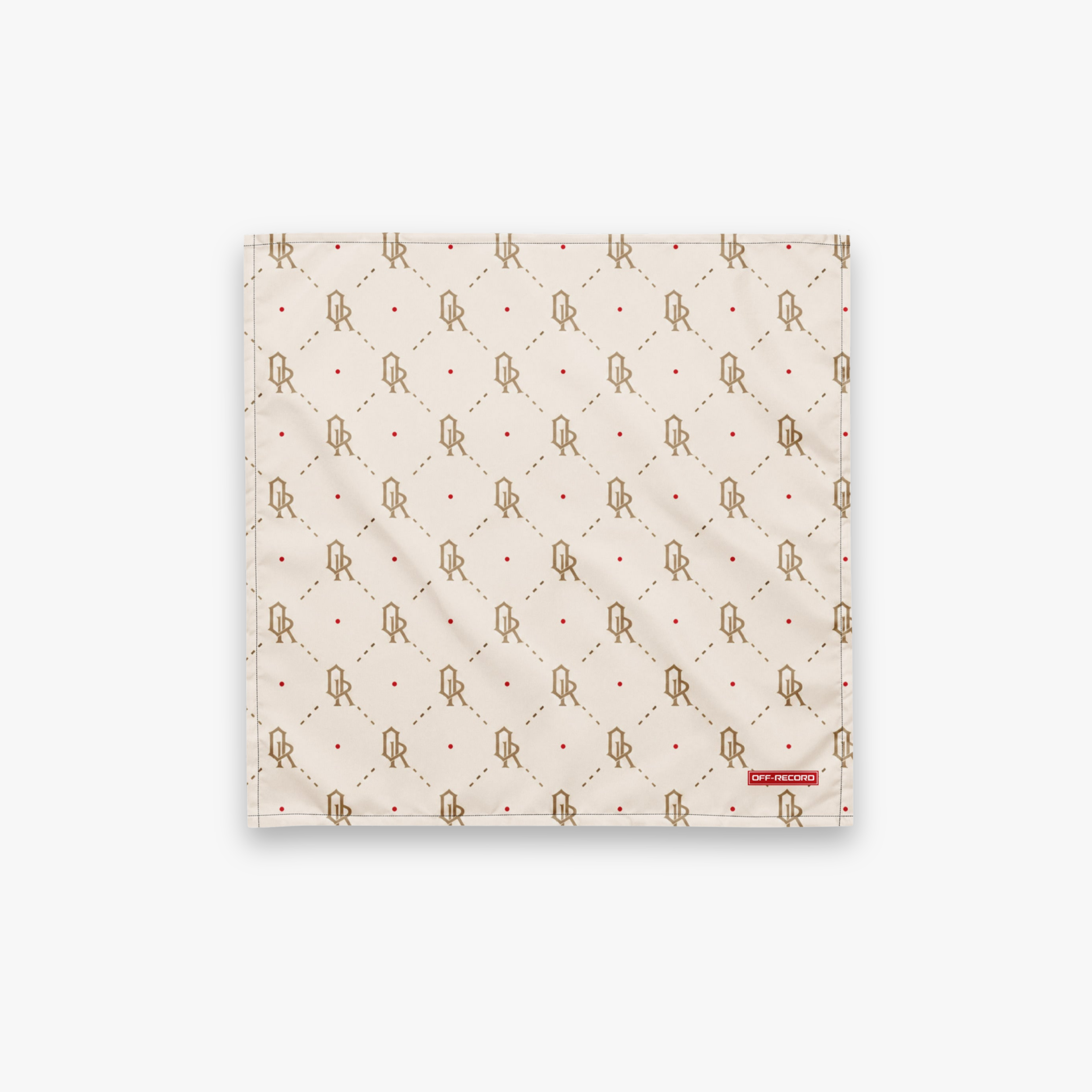 A square cream-colored fabric accessory, likely a pocket square or scarf, featuring a repeating brown monogram pattern with red dots and a small red brand tag on the bottom right.