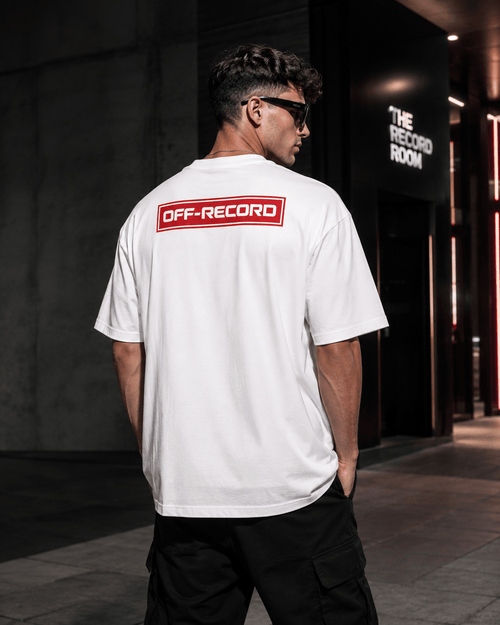Person wearing a white Off-Record reverse stamp tee logo t-shirt with 'OFF-RECORD' logo on the back, standing in an urban setting.